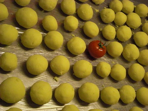 Viele vorbereitete Kartoffelknodel auf einer Edelstahl Platte - in der Mitte liegt eine Tomate