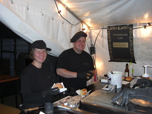 Ann-Karin (links) und Dennis (rechts) beim belegen von Lachsbrötchen. Im Hintergrund ein Schild mit der Aufschrift Flammlachs 3,50€