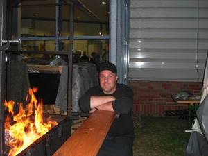 Dirk stützt sich mit dem Oberkörper auf die Seitenablage des Lachsgrills in dem ein Feuer brennt