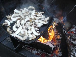 Eine Gusspfanne mit Pilzen über dem Feuer