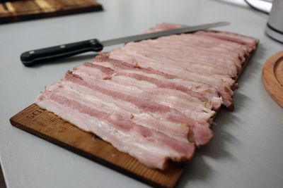 Selbstgemachter Bacon in Scheiben auf einem Holzbrett mit Messer