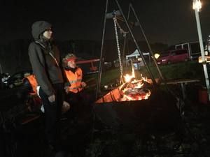 Feuerschale mit Dreibein am Abend, daneben stehen zwei Personen