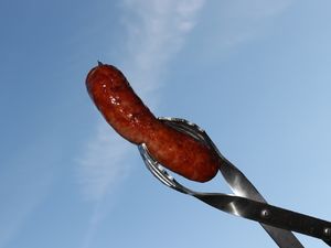 Smoked Sausage in der Grillzange vor blauem Himmel