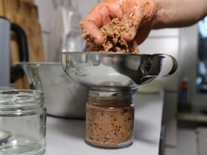 Wurstmasse wird mit einem Trichter in Gläser gefüllt