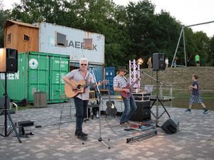 Zwei Musiker mit Gitarren spielen vor Containern