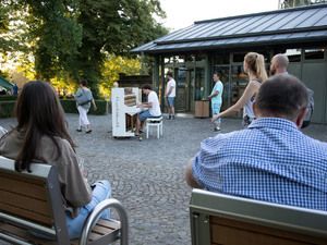 Besucher auf Bänken vor einem Klavier auf dem Platz