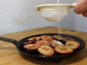 Puderzucker wird über die Pflaumenhälften gesiebt