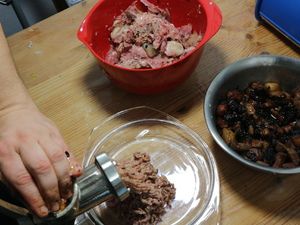 Fleisch wird durch den Fleischwolf gedreht, daneben die Apfel-Speck-Mischung