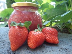 Glas Erdbeermarmelade mit drei Erdbeeren davor