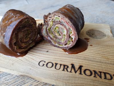Aufgeschnittene Rinderroulade mit Füllung in Sauce auf einem GourMonds-Brett