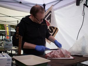Teammitglied mit Handschuhen schneidet ein Stück Fleisch zu