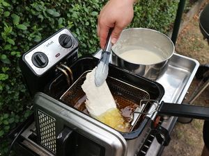 Fischfilet wird durch den Teig gezogen und in die Fritteuse gelegt