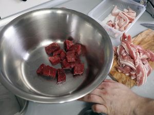 Fleischwürfel in einer Edelstahlschüssel, daneben Speck