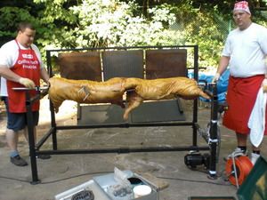 Dennis (links) und Hendrik (rechts) montieren einen Spieß mit Zwei Schweinen auf einen Schweinegrill
