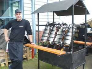 Teammitglied neben dem Lachsgrill mit eingespannten Lachshälften