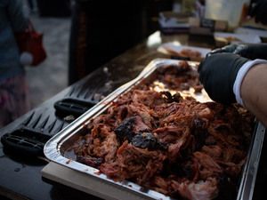 Pulled Pork in einer Aluschale wird mit Handschuhen zerpflückt