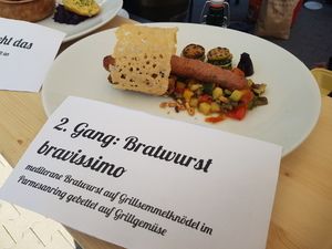 Menükarte zweiter Gang „Bratwurst bravissimo“ vor dem Teller
