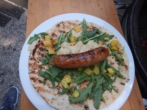 Fladenbrot mit Rucola, Ananas und Bratwurst vor dem Aufrollen