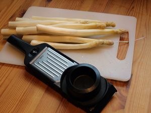 Spargel und Gemüsehobel auf einem Schneidebrett