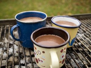 Drei Emaillebecher mit heißer Schokolade auf dem Grillrost