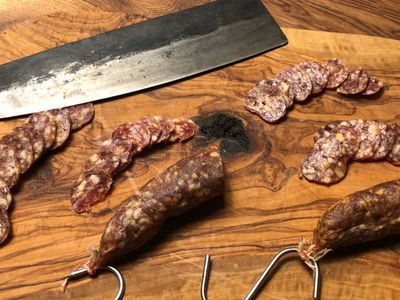 Salamischeiben und ganze Salami mit Hackmesser auf Olivenholz